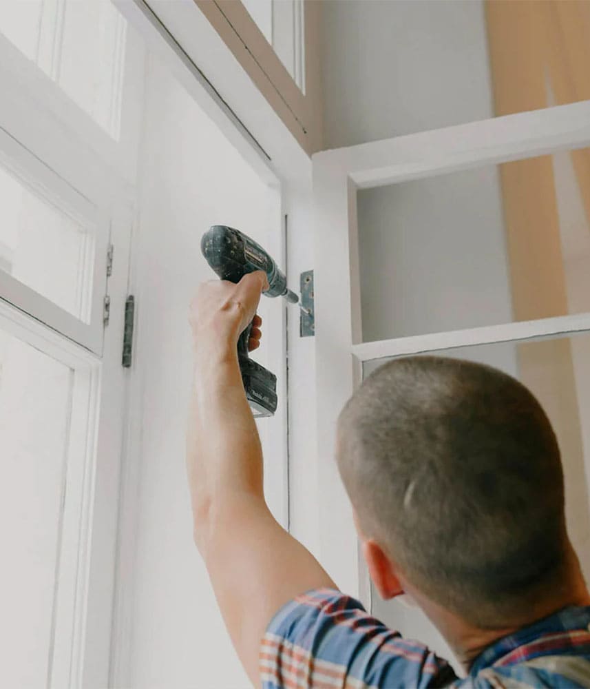 Un homme utilise une perceuse pour fixer un cadre de fenêtre
