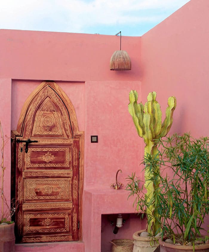 Porte en bois sculpté dans un mur rose avec cactus